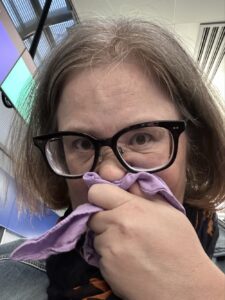 A woman in glasses, sniffling into a purple handkerchief