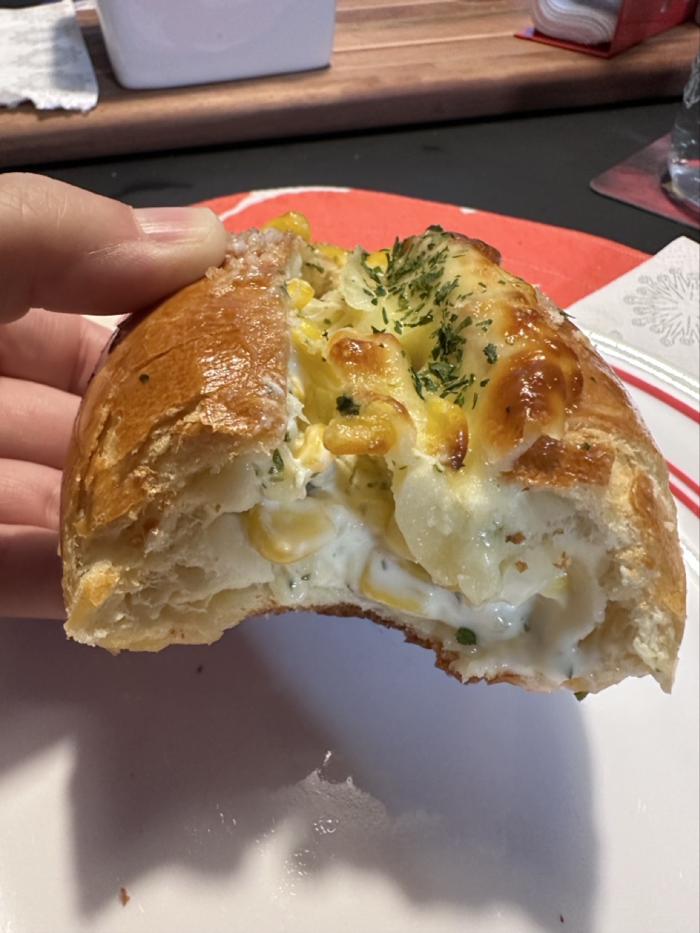 A half-eaten corn cheese salt bread, showing an interior filled with melted cheese and sweet corn