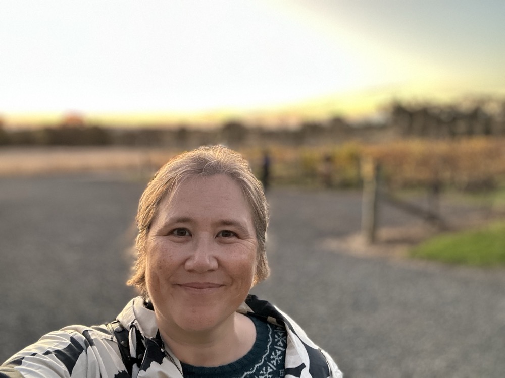 A person smiling at a vineyard at sunset