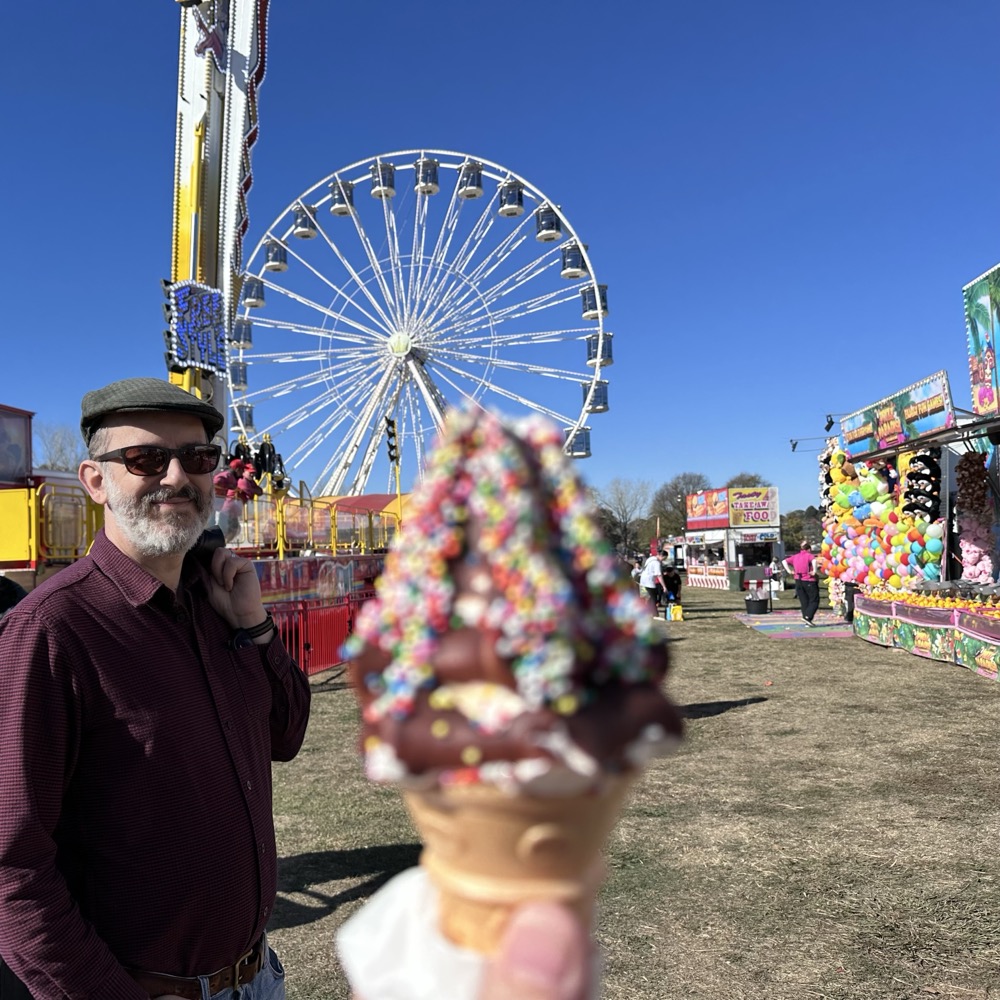 A person holding an ice cream with a Ferris wheel behind