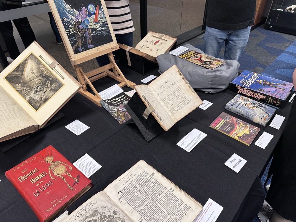 A table covered in rare books, including early illustrated French editions of "The War of the Worlds," different versions of "Starship Troopers" (including a board game!), and the very first comic book featuring Spider-Man