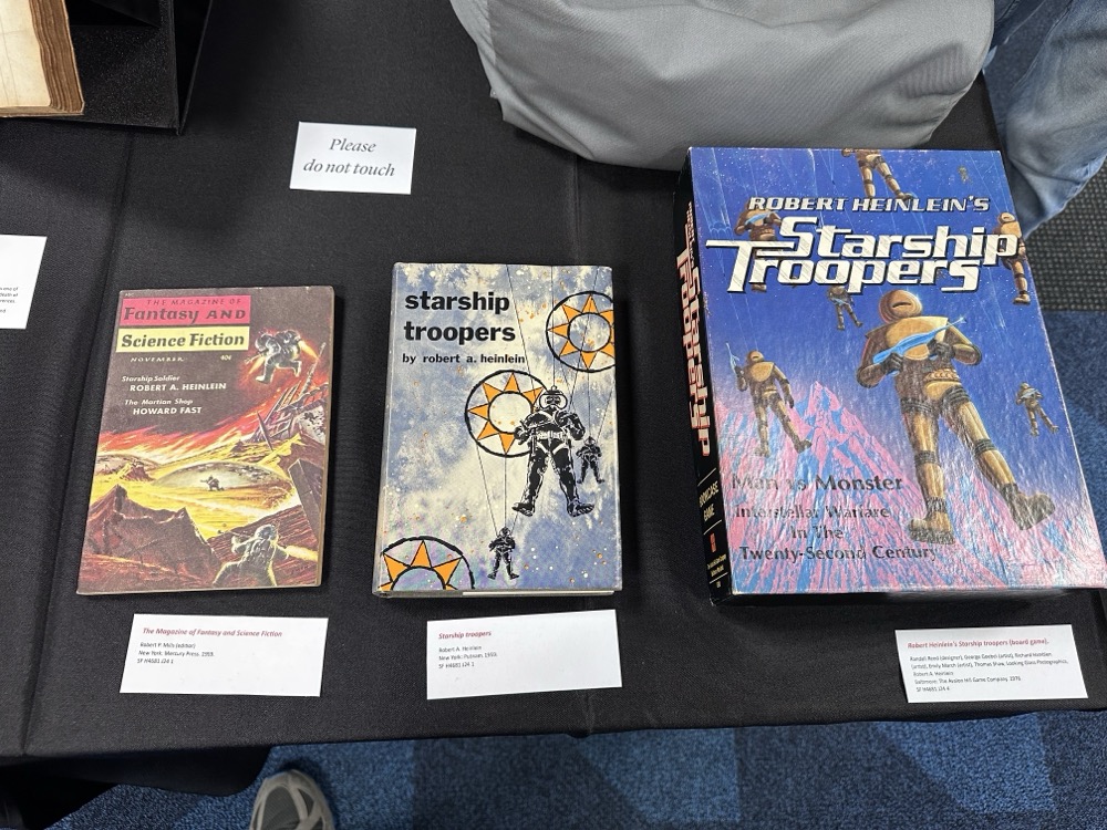 Three items: A copy of "The Magazine of Fantasy and Science Fiction" featuring a story called "Starship Soldier"; a first edition of "Starship Troopers"; and a board game version of Starship Troopers.