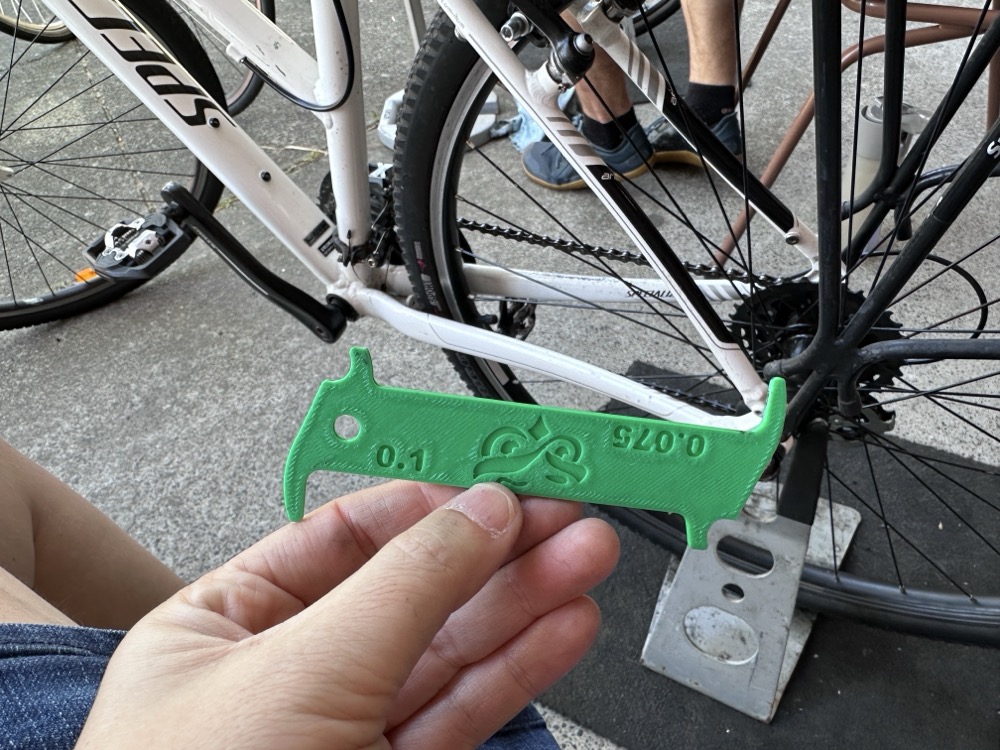 A person holding a green piece of plastic with small nubs on each end, in front of a bicycle