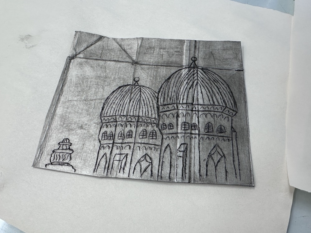 A piece of silver Tetrapak inscribed with a rough sketch of the towers of the Frauenkirche, two domes on top of stone towers