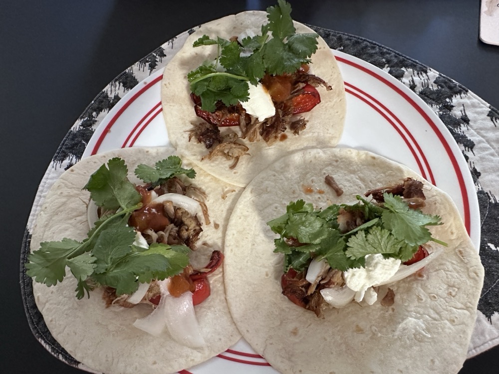 Three "street taco" torillas with pork carnitas, grilled capsicum, onions, salsa, coriander, and sour cream.