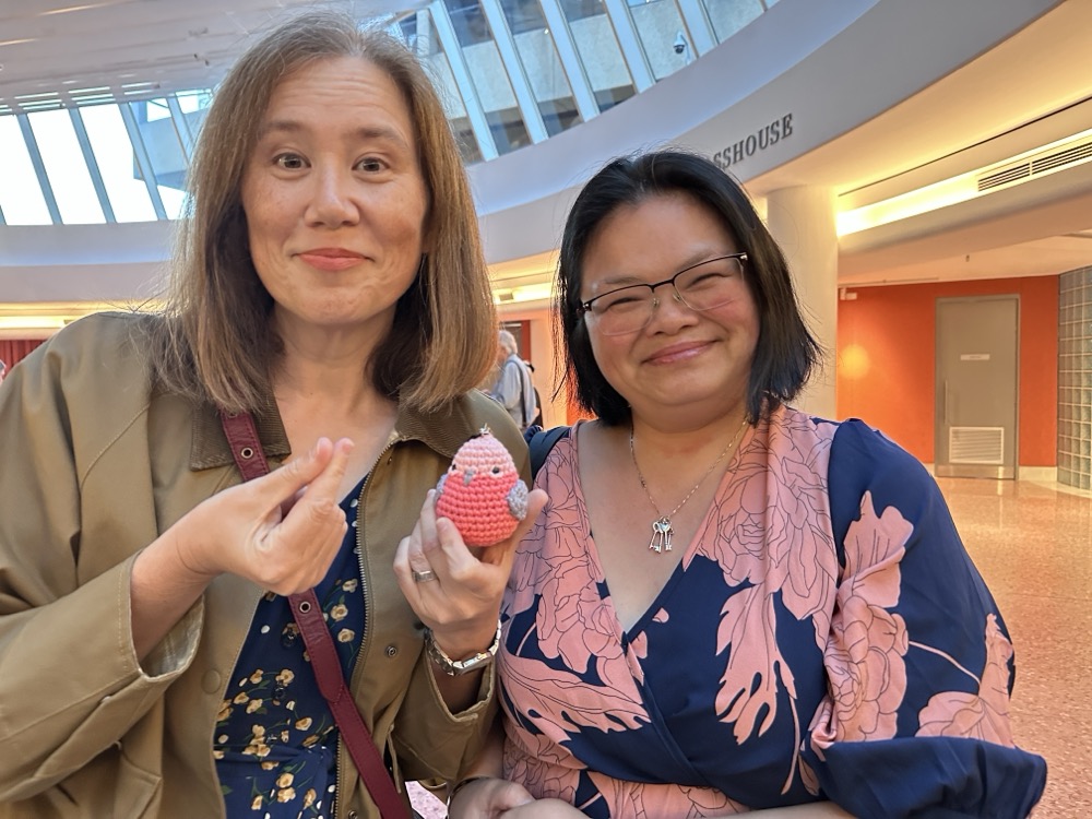Two women, one of which is holding a small round pink crocheted bird.