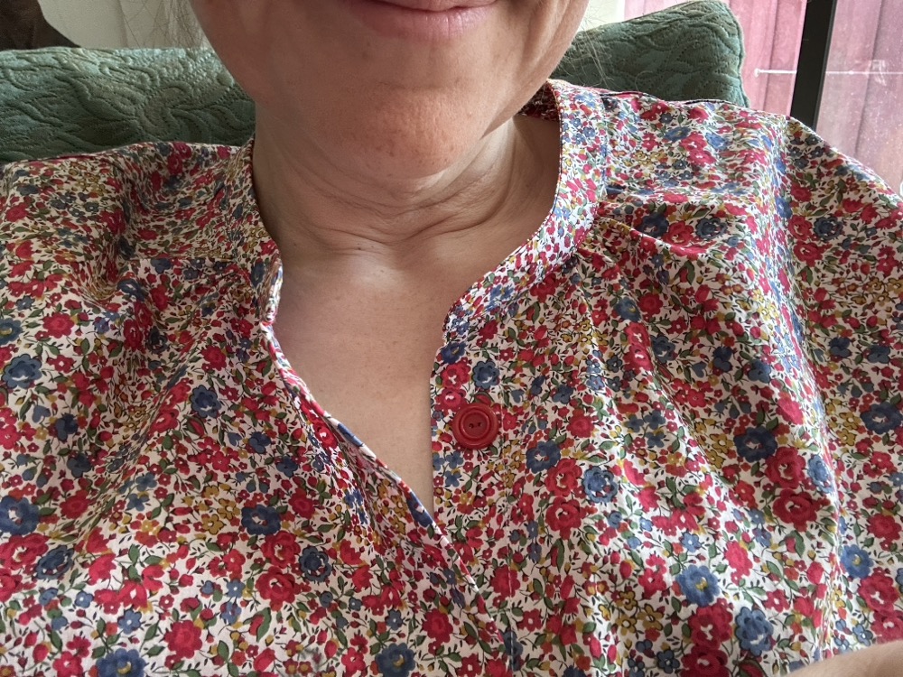 A closeup of the collar of a woman wearing a blouse with an allover print of tiny red, blue, and yellow flowers
